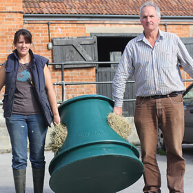 Two people carrying a Hay Hutch filled with hay